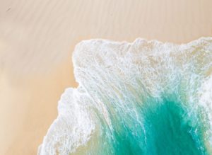 Vue aérienne d'une vague turquoise s'écrasant sur une plage de sable immaculée.