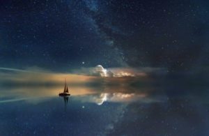 Un voilier flotte paisiblement sur l’eau sous un ciel étoilé, créant une ambiance apaisante et sereine.