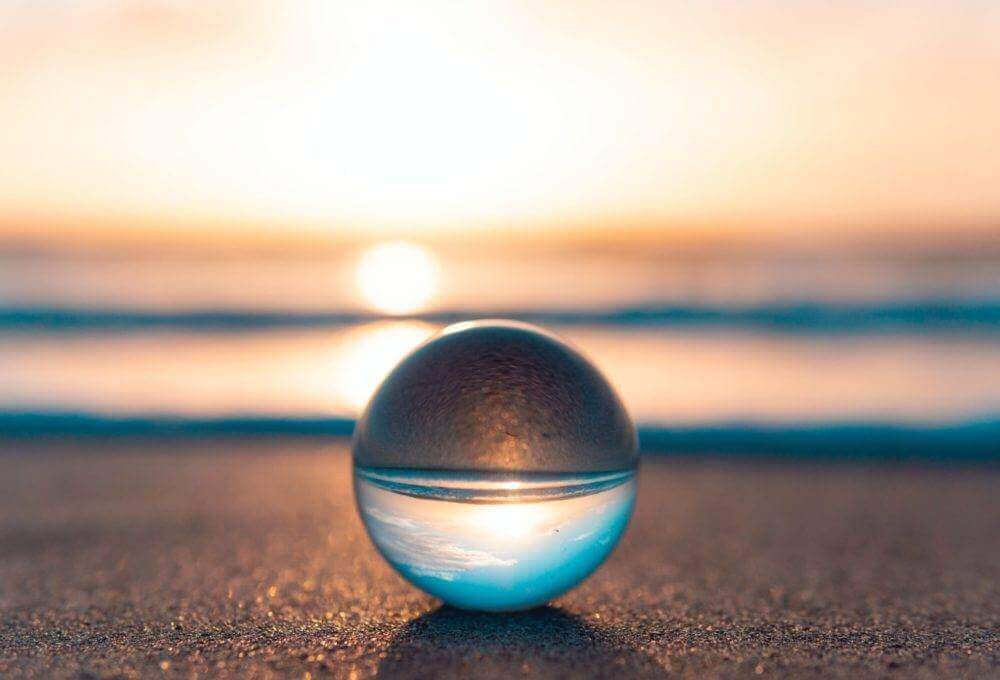 Une boule de verre posée sur la plage au coucher du soleil, rayonnant de quiétude et de sérénité grâce à la sophrologie.
