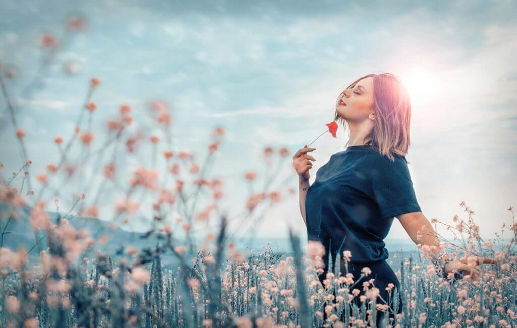 Une femme se tient dans un champ avec une fleur dans sa main, cherchant à combattre son stress.