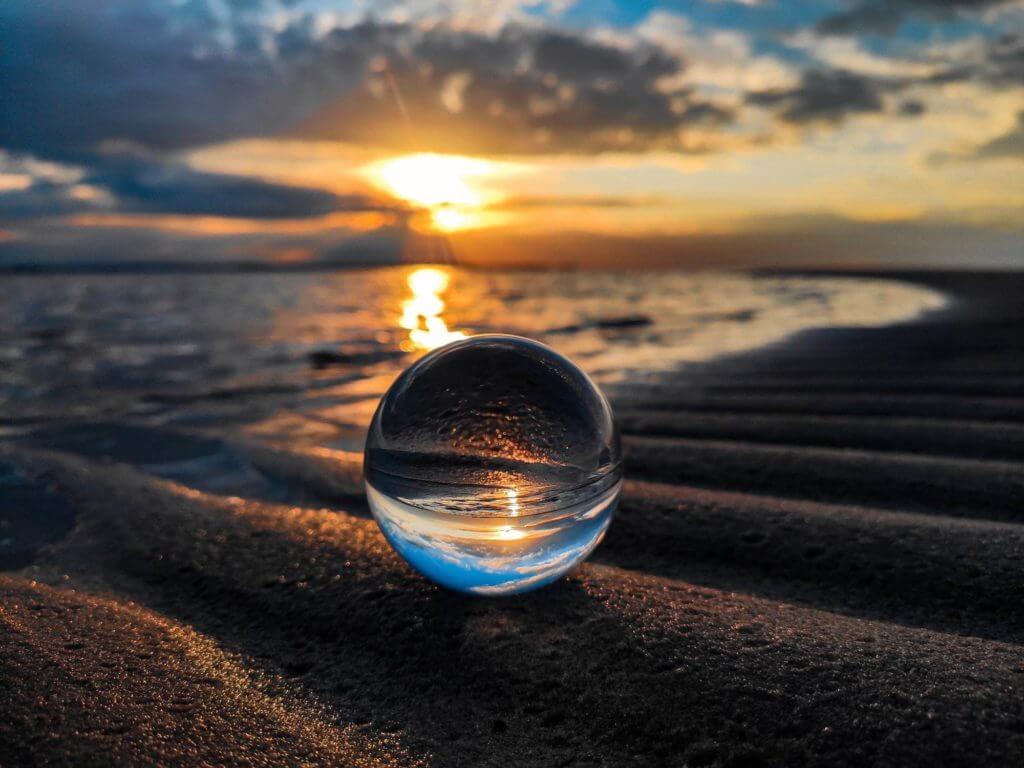 Une boule de verre posée sur le sable au coucher du soleil crée une ambiance sereine pour les praticiens de la sophrologie.