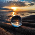 Une boule de verre posée sur le sable au coucher du soleil crée une ambiance sereine pour les praticiens de la sophrologie.