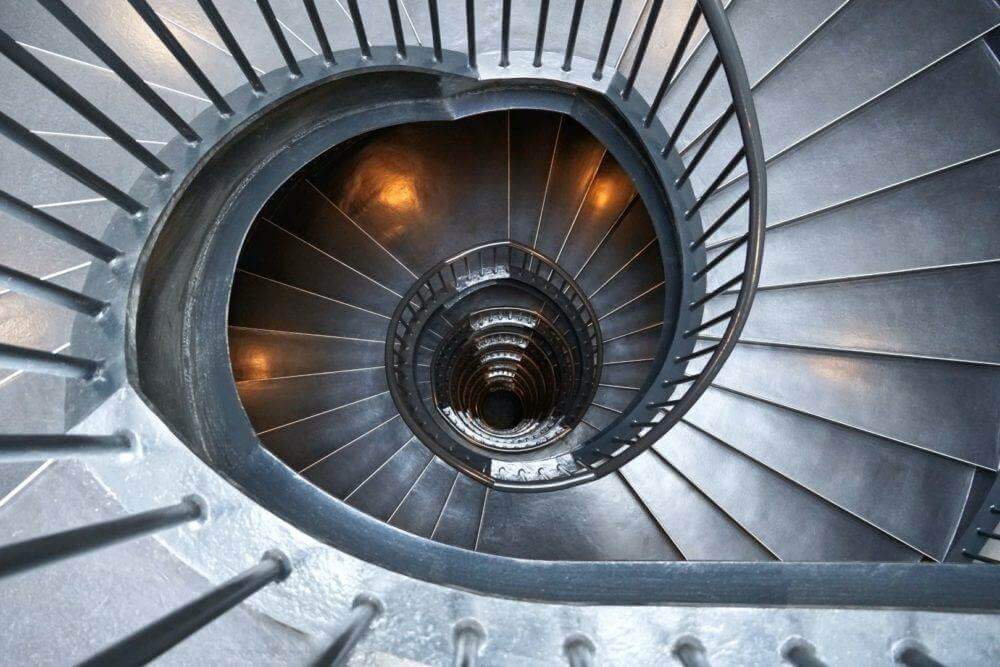 Un escalier en colimaçon hypnotique dans un immeuble aux garde-corps métalliques.