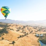 Une montgolfière colorée survole un champ tandis que les passagers sont fascinés par les vues hypnotiques.