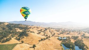 Une montgolfière colorée survole un champ tandis que les passagers sont fascinés par les vues hypnotiques.