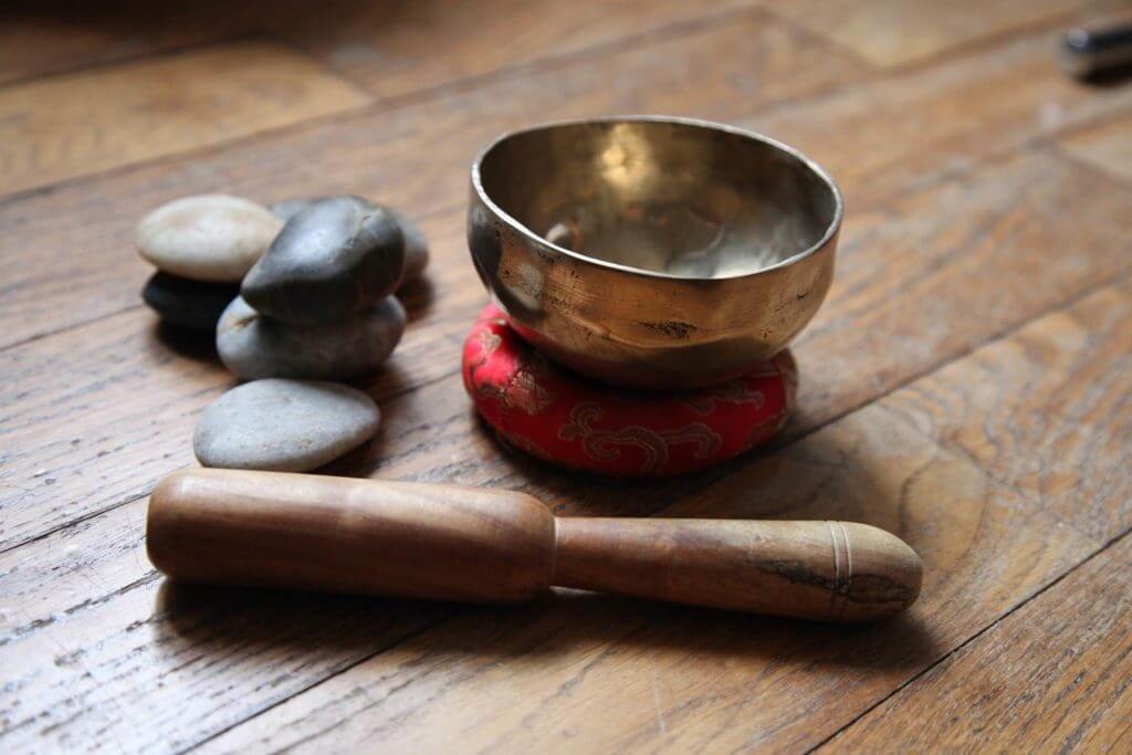Un bol chantant en bois et une pierre sur un plancher en bois, parfait pour les amateurs de musicothérapie ou ceux intéressés par les bols tibétains.