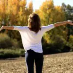 Une femme pratiquant la sophrologie les bras en l’air.
