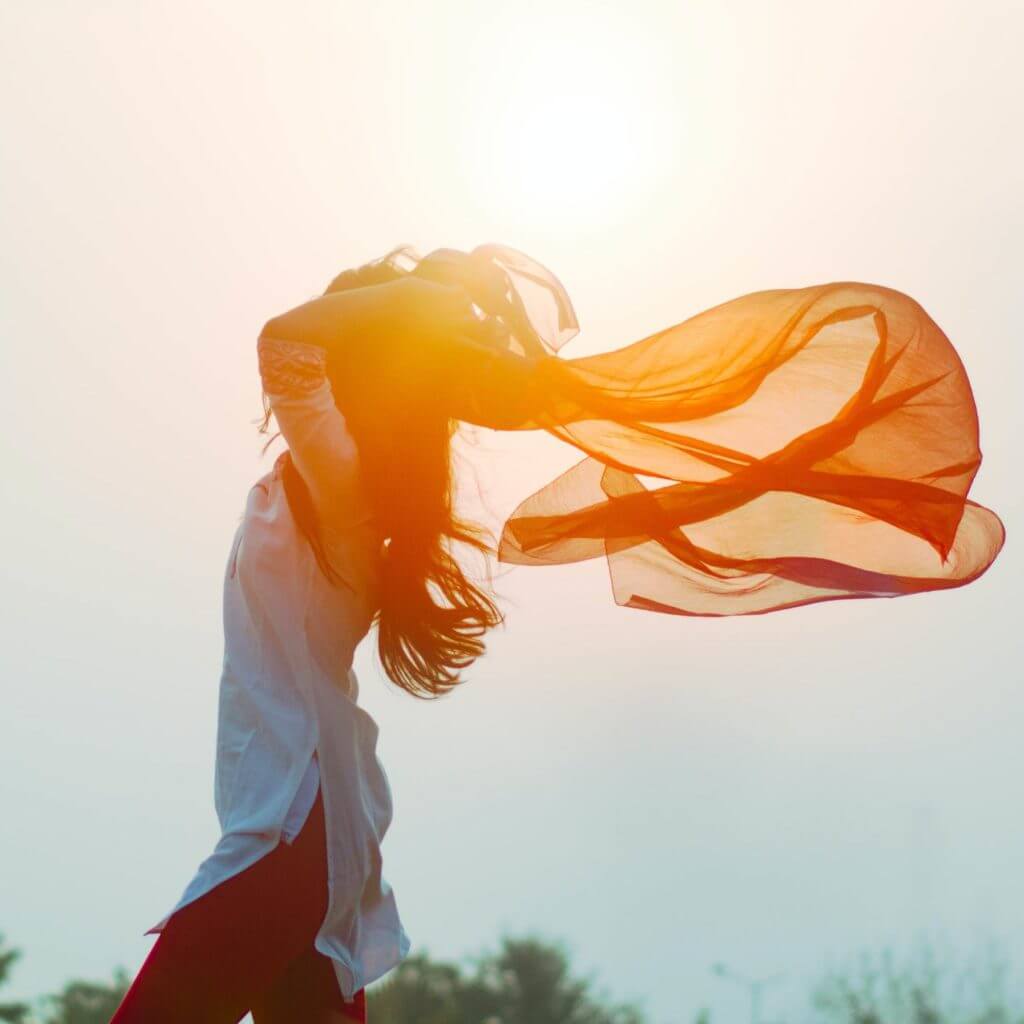 Une femme avec un foulard flottant au vent, affichant sa silhouette élancée obtenue grâce au pouvoir de l'hypnose et des techniques de perte de poids.