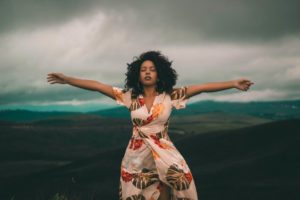 Une femme en robe à fleurs debout sur une colline, les bras tendus, souffrant de phobie.