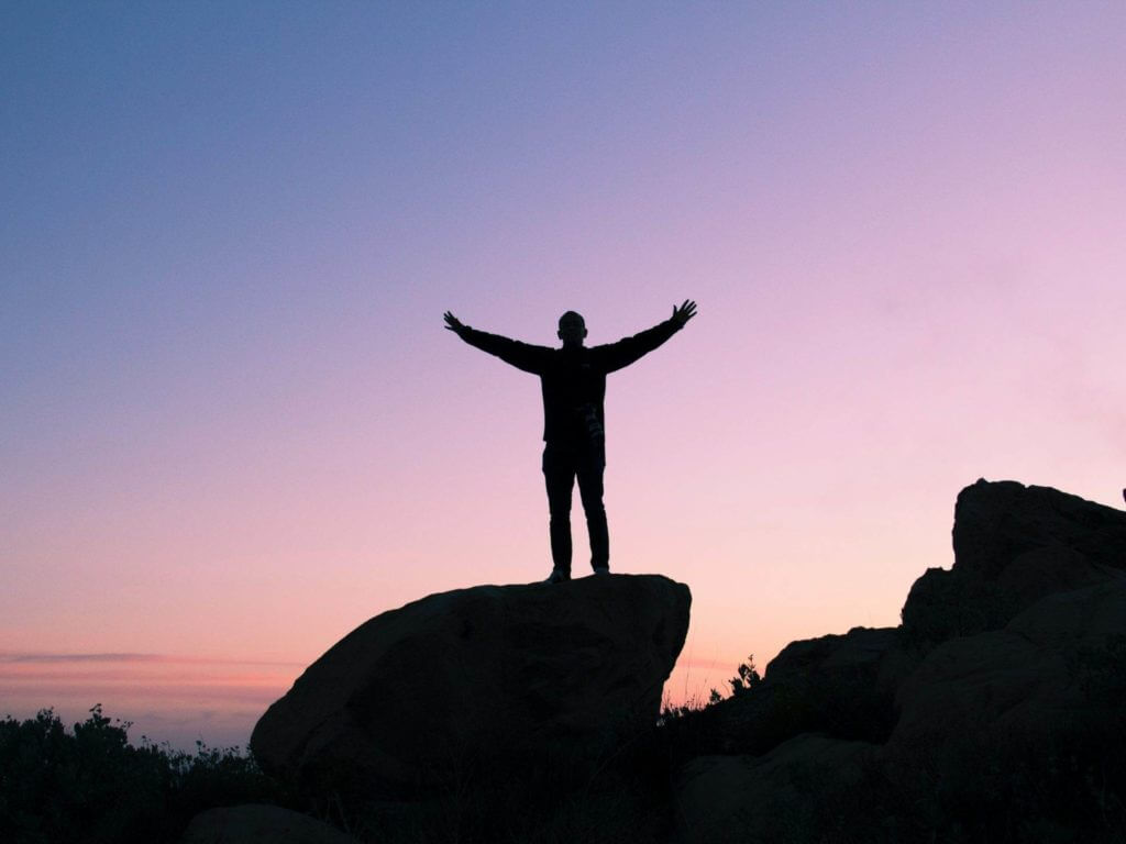 Une silhouette d’homme debout au sommet d’un rocher au coucher du soleil, en état d’hypnose.