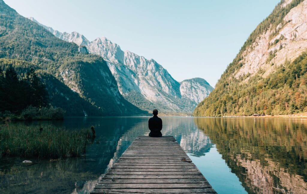 Un homme paisiblement assis sur un quai, profitant d’une vue fascinante sur un lac serein.