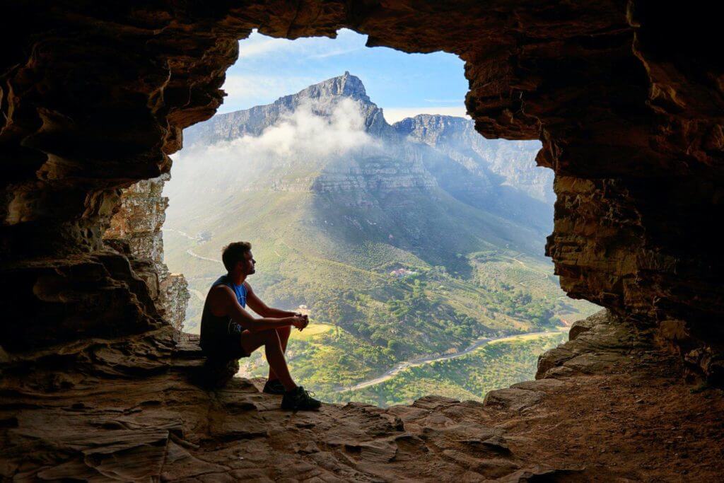 Un homme pratiquant la sophrologie en regardant hors d'une grotte.