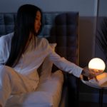 Une femme est assise sur un lit en état d’hypnose avec une lampe devant elle.