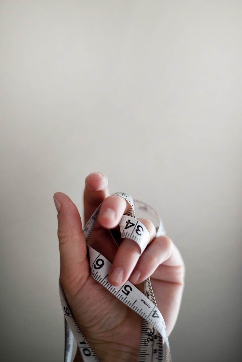 La main d'une personne tenant gracieusement un ruban à mesurer, le guidant doucement autour de sa taille alors qu'elle se lance dans un voyage pour maigrir (perdre du poids) à l'aide de l'hypnose (