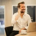 Un homme parle au téléphone alors qu’il est assis à un bureau.