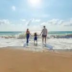 Une famille se tient sur la plage, les mains dans le sable.