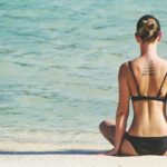 Une femme assise sur la plage avec un tatouage sur le dos.