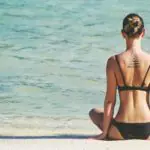 Une femme assise sur la plage avec un tatouage sur le dos.