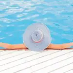 Une femme au chapeau se repose au bord d’une piscine.
