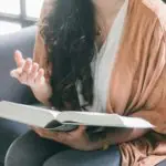 Une femme est assise sur un canapé en train de lire un livre.