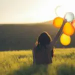 Une femme tenant des ballons dans un champ au coucher du soleil.