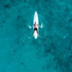 Une vue aérienne d’un homme chevauchant une planche de surf dans l’océan.